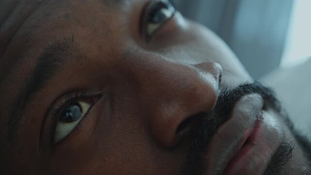 Close-up view of face of young African American man sleeping in bed at home, then waking up and opening his eyes