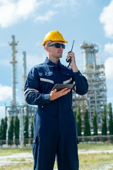 Vertical image of factory engineer or technician worker man hold walkie-talkie also hold tablet in other hand and stand in front of refining and petrochemical factory with day light.