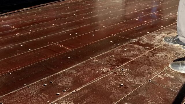 Smartly uniformed Employee meticulously maintains wooden teak decking at a commercial establishment, showing his professionalism and pride in the work place