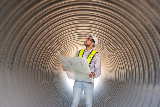 Young mechanical engineer holding blueprint drawing to checking and inspection pipeline system new construction project of industrial.