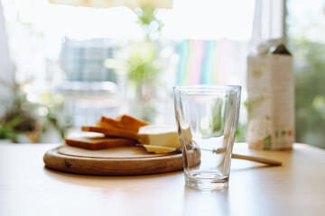 An empty glass stands on table, in background there is bread, butter, milk. Breakfast