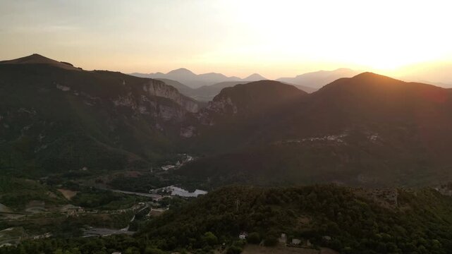 A stunning drone view of Frasassi Gorge, Italy, at sunset. Golden light bathes the cliffs and river, creating a serene, awe-inspiring landscape as the day fades into a warm, tranquil evening.