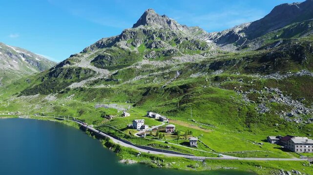 A stunning drone view over the Spl&uuml;gen Pass, capturing crystal-clear alpine lakes surrounded by towering mountains. The serene landscape showcases nature's beauty at the border of Switzerland Italy