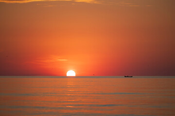 Obraz premium Sun rising from the water at the Black Sea with boat