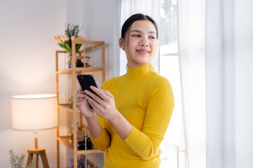 Happy young asian woman relax on comfortable couch at home texting messaging on smartphone, smiling girl use cellphone, chatting online message, shopping online from home
