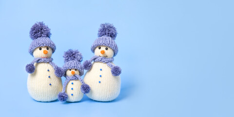 Family of knitted snowmen celebrate the holidays on blue background. Winter fairy tale story with your own hands, hobby. Merry Christmas and New Year 2025 greeting card. Banner