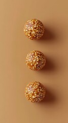 Three spherical granola bites arranged in a vertical line on a beige background, showcasing a healthy snack option.