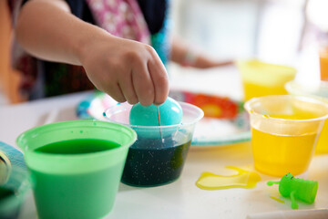 Child's hand dipping an Easter egg in colorful dye cups