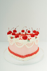 Heart-shaped pink cake with whipped cream and cherries