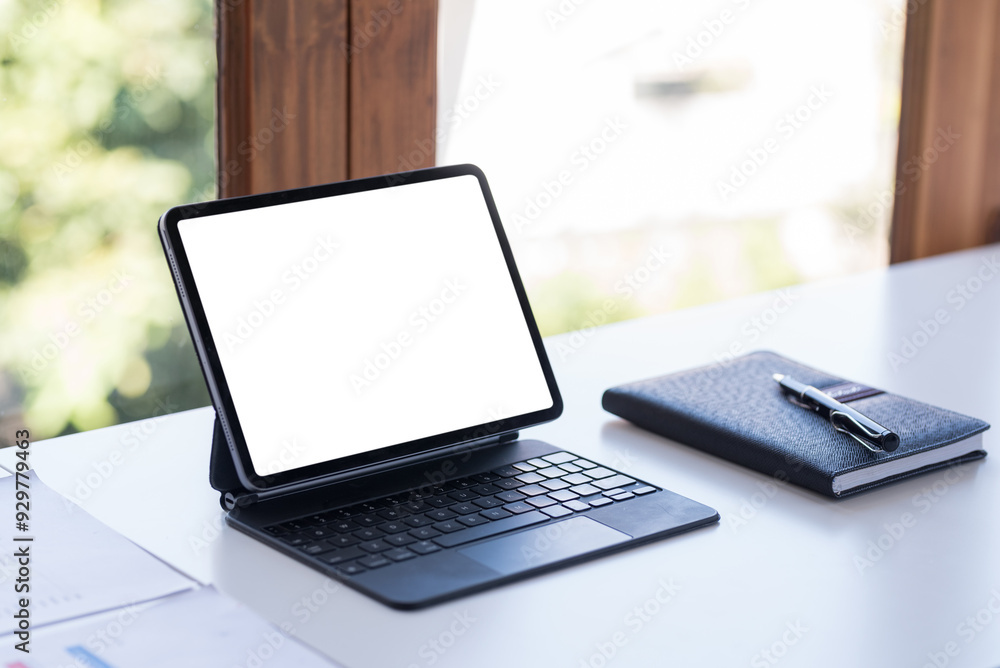 Poster tablet is displaying a white screen for your advertisement on a work desk with a notebook and a pen 