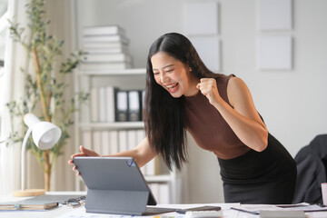 Businesswoman feeling happy about good news received on digital tablet, raising her arm with excitement