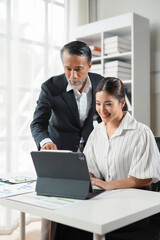 Senior manager mentoring a young employee, pointing at a digital tablet while working together on a new project in the office
