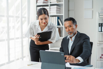 Businessman and businesswoman discussing work using digital tablet and clipboard in modern office