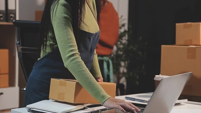Startup SME small business entrepreneur of freelance Asian woman wearing apron using laptop and box to receive and review orders online to prepare to pack sell to customers, online sme business ideas.