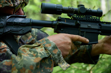 Hunter with rifle wearing camouflage suit sitting in ambush. Camouflaged sniper in the forest in...