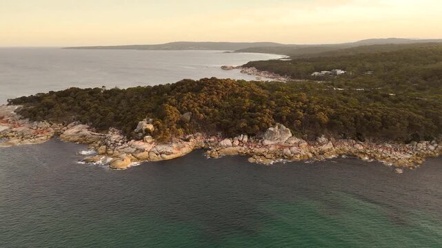 Aerial backwards shot of rocky coastline in Tasmania during sunset time. Bay of Fires in Australia. Wide shot.