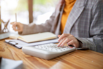 Fototapeta premium A close-up image of a businesswoman using a calculator and taking notes in her notebook.