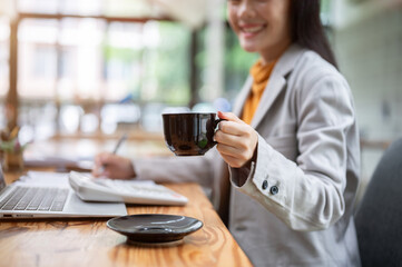 An Asian businesswoman holding a coffee cup, drinking coffee while working on her task in the office