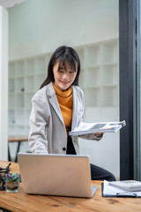 A beautiful Asian businesswoman is leaning against the table, working on her laptop.