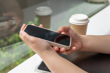 A close-up side view image of a woman using her smartphone while sitting in a coffee shop.