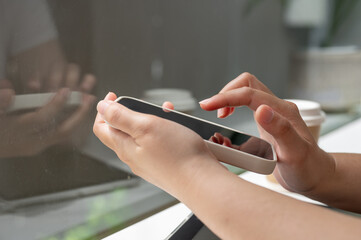 A close-up side view image of a woman using her smartphone while sitting in a coffee shop.