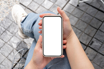 Top view image of a woman in jeans sitting outdoors and using her smartphone.