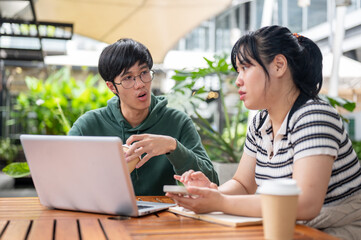 A serious young Asian man is explaining work to his friend, working on a co-project together.