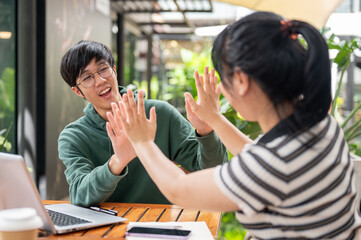 Two cheerful young Asian friends are giving high fives to each other, celebrating good news together