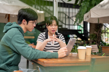 A positive Asian woman is working on a co-project with her friend, showing something on her laptop.