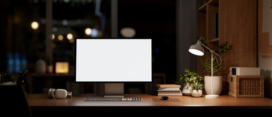 A modern dark office at night, a computer mockup on a desk, illuminated by a table lamp.