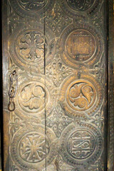 Beautiful carved wooden door in the wall of a medieval church. Patterns of a cross and grapevine placed in a circle. old rusty iron handle