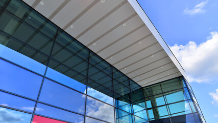 Fragment of a modern building made of steel and glass. Abstract modern commercial architecture fragment. Walls made of shiny glass and steel under blue sky.