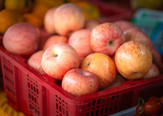 Red basket of fresh apples on a wooden table in a fodd market.
