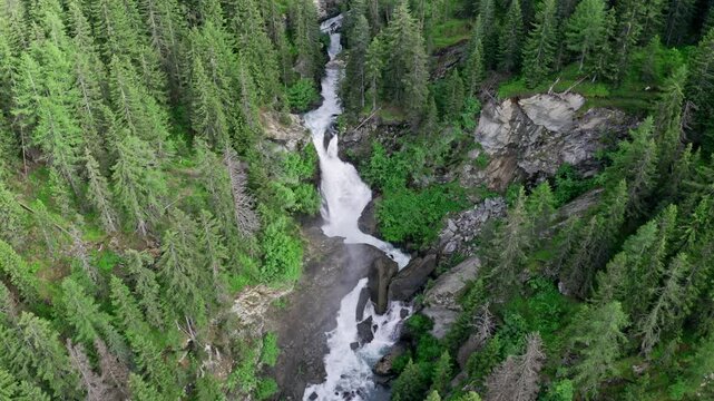Cascate del rutor waterfall surrounded by lush green pine trees in a dense forest, aerial view