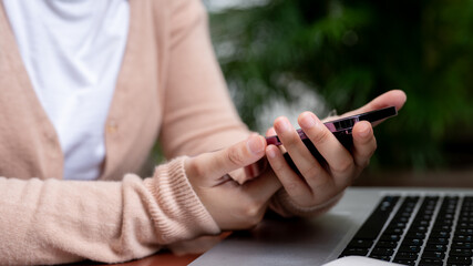 A close-up image of a woman is using her smartphone while working remotely at a table in a garden.