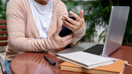 A cropped image of a woman using her smartphone at a table outdoors, checking messages.