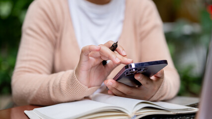 A close-up image of a woman using her smartphone while holding a pen, browsing the internet.