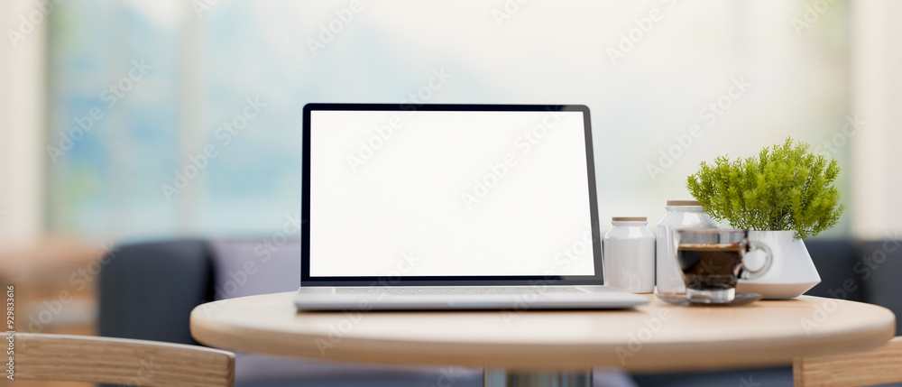 Poster a laptop computer with a white-screen mockup on a round wooden table in a minimalist cafe.