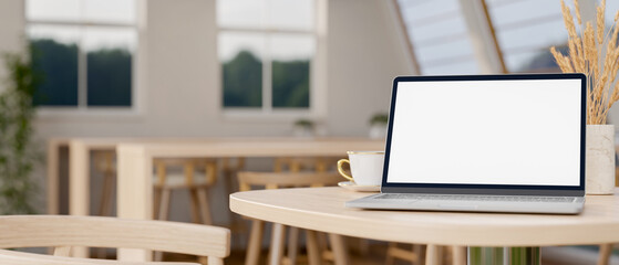 A laptop computer on a wooden table in a contemporary, minimalist co-working space.