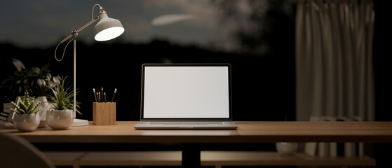 A laptop mockup on a table in a modern dark room at night, illuminated by a table lamp.