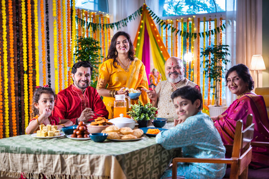 Portrait of happy Indian family in traditional outfit celebrating Diwali together at home eating food.