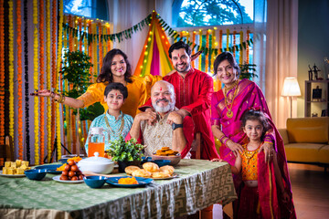 Portrait of happy Indian family in traditional outfit celebrating Diwali together at home eating food.