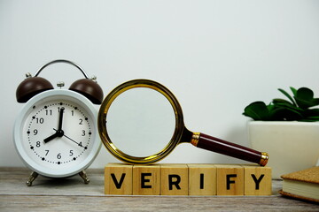 Magnifying glass and alarm clock with wooden blocks alphabet letters VERIFY text message on wooden...