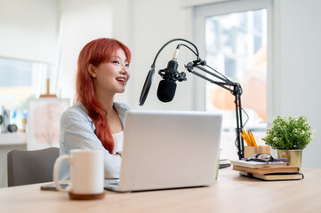 A beautiful Asian female podcaster is working in her studio, speaking into a microphone.