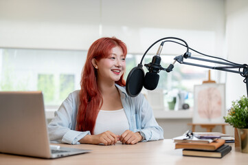 A beautiful Asian female podcaster is working in her studio, speaking into a microphone.