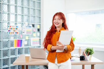 A confident female graphic designer stands in her studio with a graphic drawing tablet in her hand.