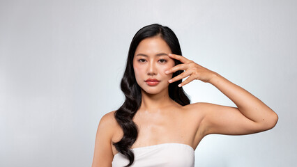 Fototapeta premium A gorgeous Asian woman poses against a grey background, touching her flawless facial skin.