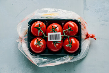 Plastic bag with red tomatoes on blue gray surface, with prominent barcode sticker
