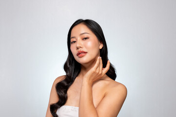 Gorgeous Asian woman with a beautiful face poses against a grey background, gently touching her chin