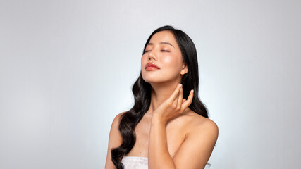 A young Asian beauty poses against a grey background, gently touching her face with her eyes closed.